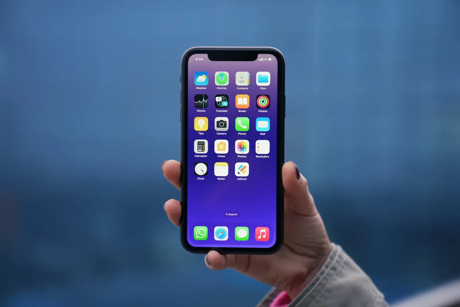 Main tenant un iPhone affichant l'écran d'accueil et ses applications